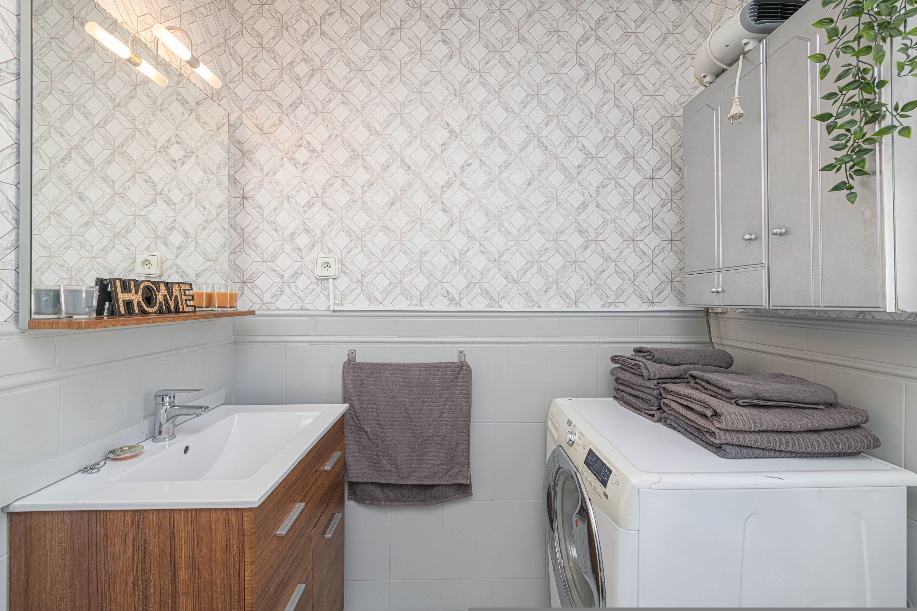 Un bagno moderno con lavandino bianco, mobile contenitore in legno, uno specchio, porta asciugamani e una lavatrice e asciugatrice impilate.