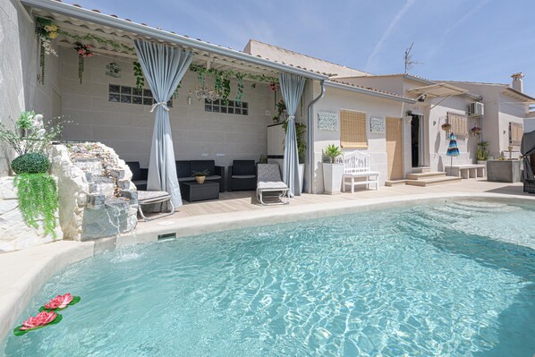 A pool area with a stone wall, lounge chairs, and a covered seating area with curtains. - Calymar in Navahermosa (Sierra de Yeguas)