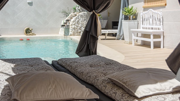 Un área junto a la piscina con una cama, una silla y vistas a la piscina.