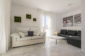 A modern living room with a white sofa, a black sofa, and a coffee table. There are two framed artworks on the wall and a window with curtains.