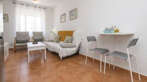 A living room with a sofa, two armchairs, a coffee table, and a small shelf with decorative items. - Apartamento Enjoy Tarifa (Tarifa)