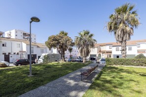 A residential area with a grassy lawn, a bench, parked cars, and a row of white buildings with tiled roofs. - Apartamento Enjoy Tarifa (Tarifa)