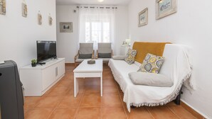 A living room with a white sofa, a TV on a white cabinet, a coffee table, and a window with curtains. - Apartamento Enjoy Tarifa (Tarifa)