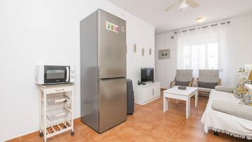 Un espacio habitable compacto con refrigerador, microondas, televisor y zona de estar.