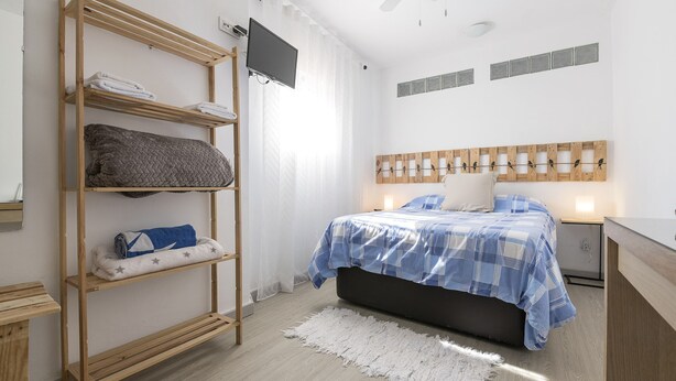 A bedroom with a bed, a wooden shelf unit, a flat-screen TV, a ceiling fan, and a bedside table. - Apartamento Enjoy Tarifa (Tarifa)