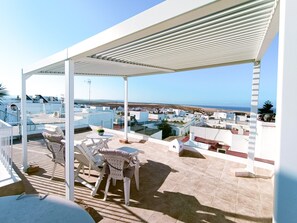 A rooftop terrace with a covered seating area, a table with chairs, and a view of the sea and buildings in the distance. - Altamar in Conil de la Frontera (Conil de la Frontera)