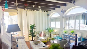 A cozy living room with a sofa, a coffee table, and a dining area with a table and chairs. There are plants, a lamp, and a window with a view. - Altamar in Conil de la Frontera (Conil de la Frontera)