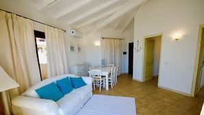 Ein geräumiger Wohnbereich mit weißem Sofa, einem Esstisch mit Stühlen und einer Küchenzeile im Hintergrund.