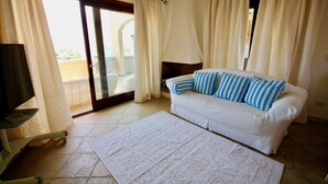 Ein Zimmer mit einer weißen Couch, gestreiften Kissen, einem Flachbildfernseher und einem großen Fenster mit Vorhängen.