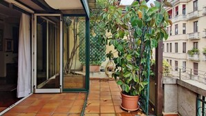 Un balcón con planta en maceta, puerta corredera de vidrio y suelo de baldosas.