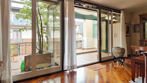 Una habitación con puerta de vidrio corredera que da a un balcón con planta en maceta y una pequeña mesa.
