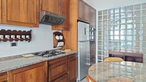 Una cocina con gabinetes de madera, un refrigerador de acero inoxidable, una estufa a gas y un protector contra salpicaduras de vidrio.