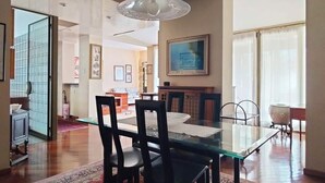 Un comedor con una mesa y sillas de vidrio, una araña y vistas de un edificio.