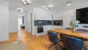 A modern kitchen with white cabinets, a wooden dining table, and a built-in oven.