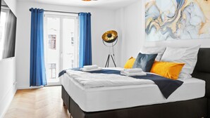 A modern bedroom with a large bed, blue curtains, a floor lamp, and a marble wall art piece.