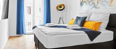 Un dormitorio moderno con una cama grande, cortinas azules, una lámpara de pie y una obra de arte de mármol en la pared.