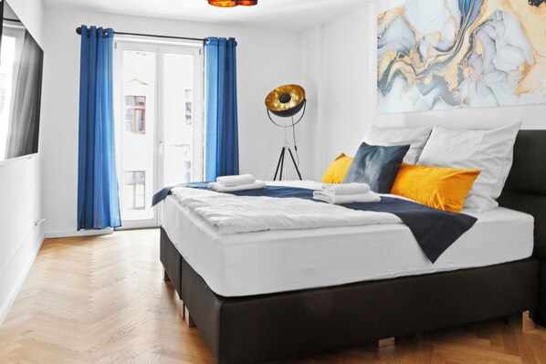 Un dormitorio moderno con una cama grande, cortinas azules, una lámpara de pie y una obra de arte de mármol en la pared.