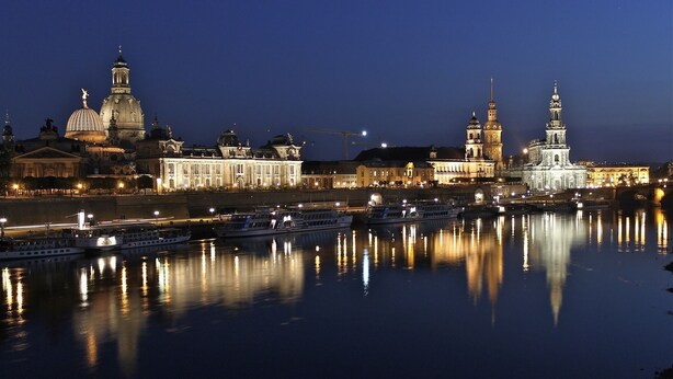 A nighttime view of a cityscape with illuminated buildings and boats on a river.