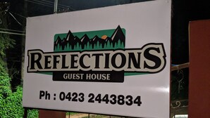 Schild für Reflections Guest House mit Berg- und Baumgrafik sowie Telefonnummer.