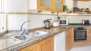 A modern kitchen with granite countertops, stainless steel appliances, wooden cabinets, and a backsplash with a floral pattern.