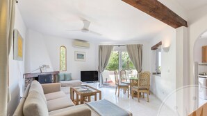 A spacious living area with a sofa, coffee table, and dining table. There is a TV, a fireplace, and a window with curtains.