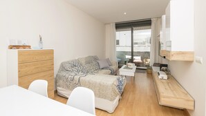 Une chambre moderne avec un canapé-lit, une commode en bois, une petite table et un bureau avec un ordinateur.