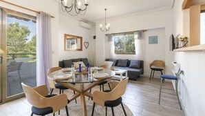 Un coin repas avec une table en verre, des chaises en bois et un tapis rond. On aperçoit un canapé et un fauteuil au fond.