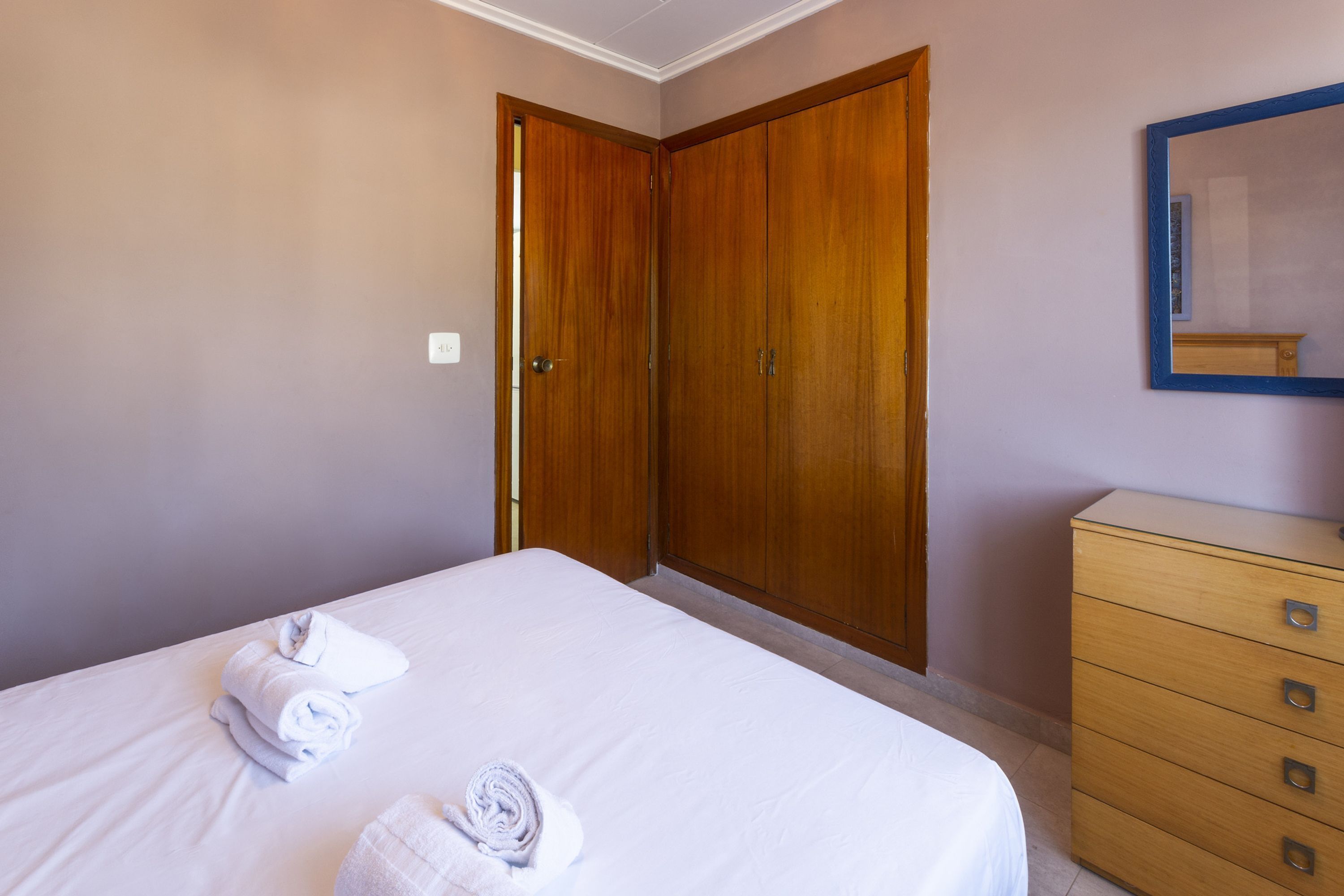Un dormitorio con una cama, dos armarios de madera, un tocador y un espejo en la pared.