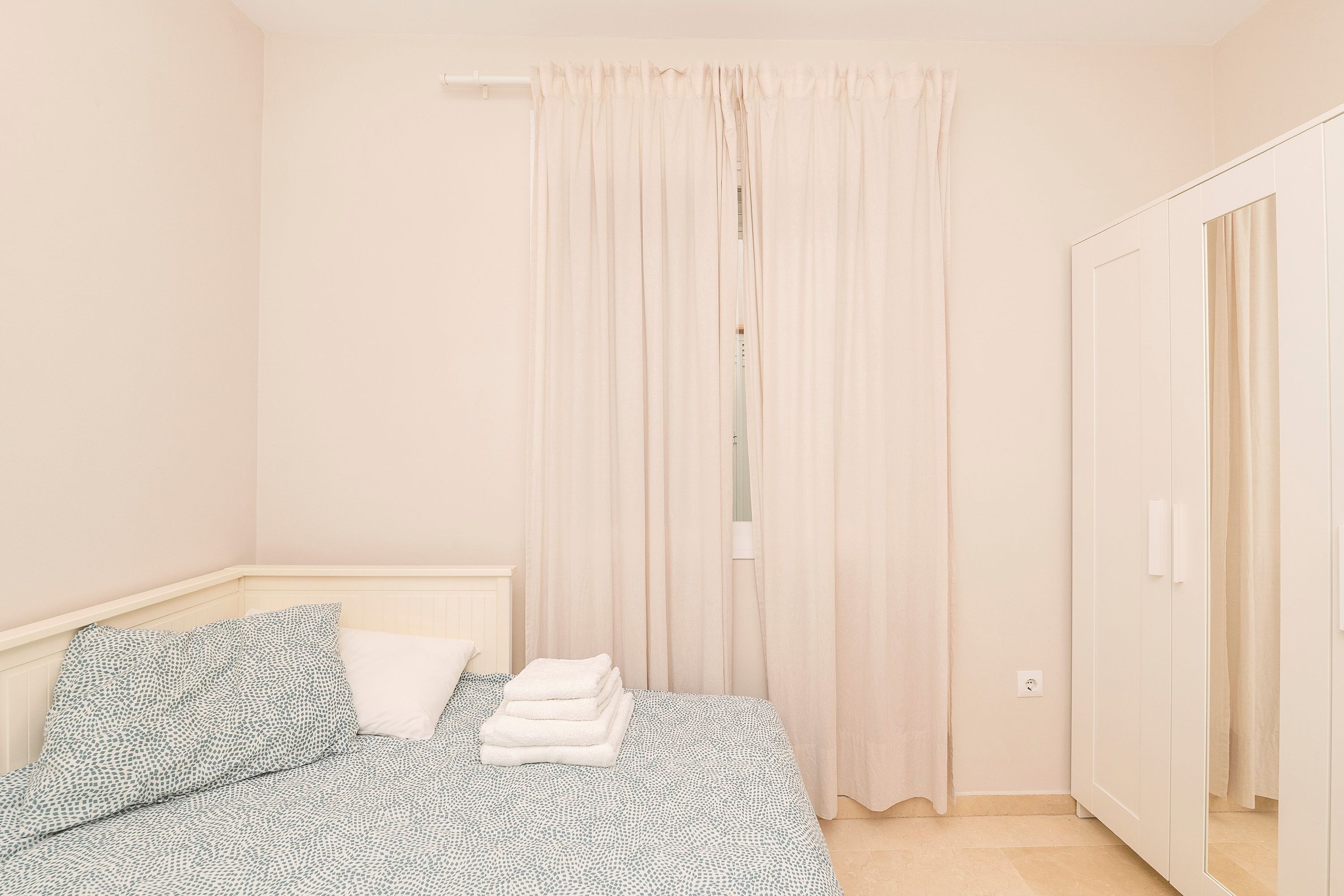 A bedroom with a bed, a wardrobe, and a window with curtains.