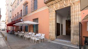 Un caffè all'aperto con tavoli e sedie bianche, un tendone rosso e un ingresso in pietra.