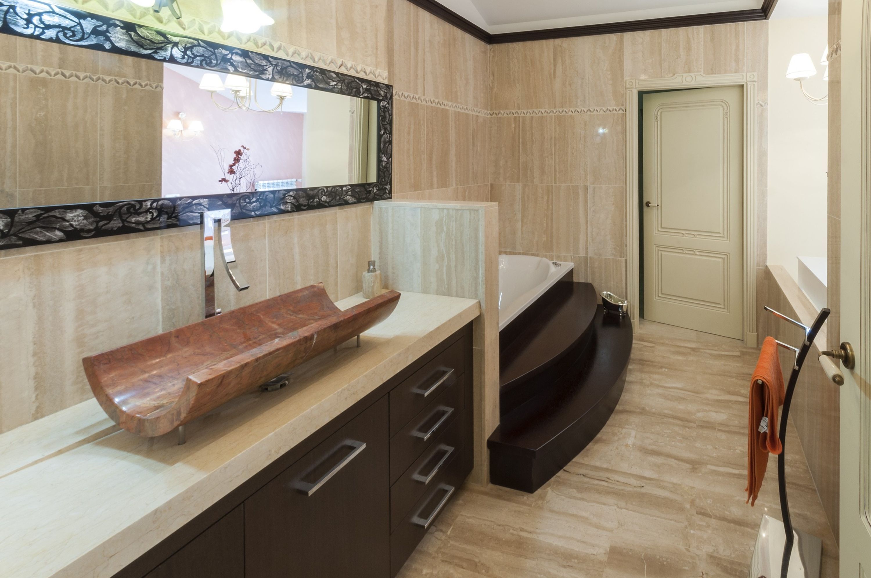 A modern bathroom with a large mirror, a wooden vanity, a bathtub, and a towel rack.