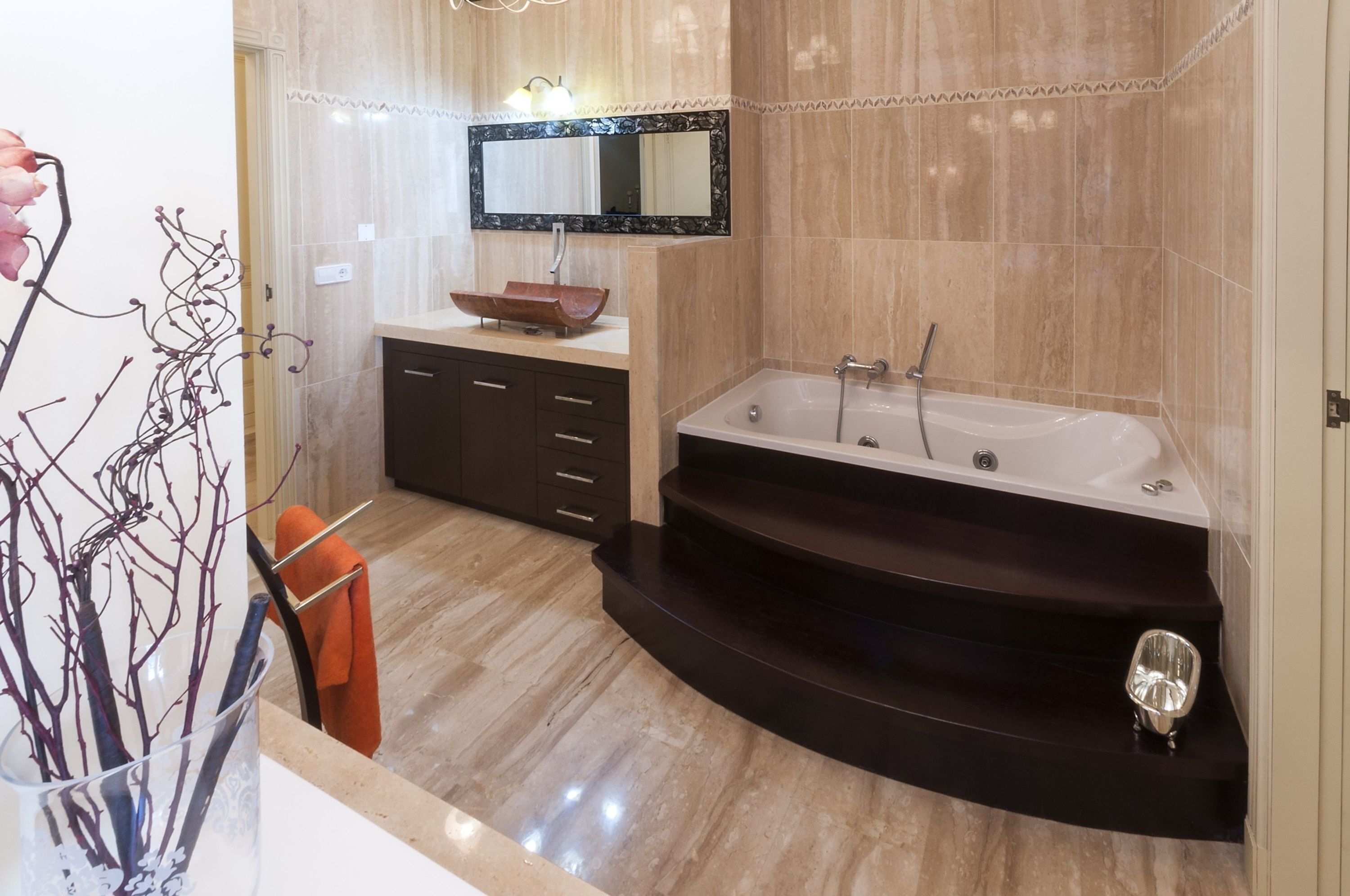 A modern bathroom with a freestanding bathtub, a vanity with a large mirror, and a decorative vase with branches.
