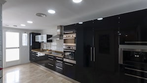A modern kitchen with black cabinets, stainless steel appliances, and a tiled backsplash. - Deseo in Grau i Platja (Gandia)