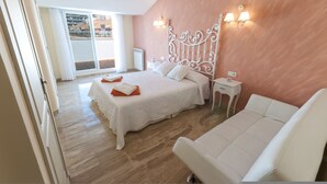 A bedroom with a large bed, a white sofa, a nightstand, and a view of the outside. - Deseo in Grau i Platja (Gandia)