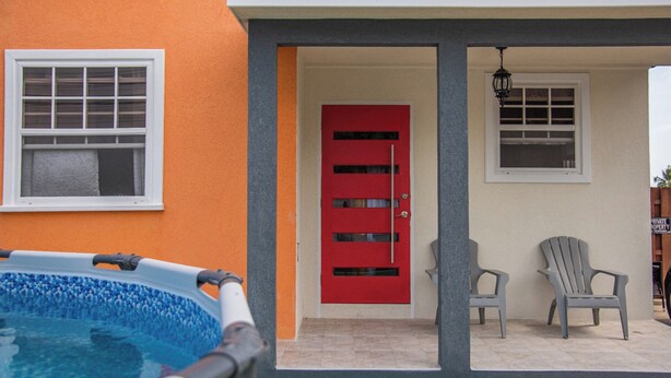 Una piscina, una porta rossa e due poltrone Adirondack all'esterno di un edificio.