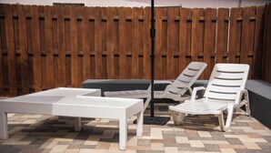 Un'area patio con un tavolo bianco, due poltrone bianche e una lampada da terra nera.