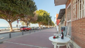 En kystpromenade med et bord og stole, en flaske vin og en rød bil parkeret langs vejen.