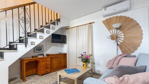 En stue med trappe, fladskærms-tv, træskrivebord, sofa og en dekorativ ventilator.
