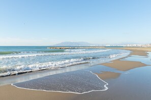 Uma praia com ondas, um cais e montanhas ao longe.