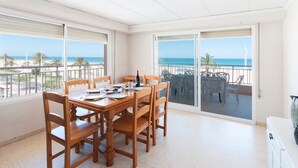 Een eetgedeelte met een tafel voor vier personen, met uitzicht op een strand en een heldere lucht.