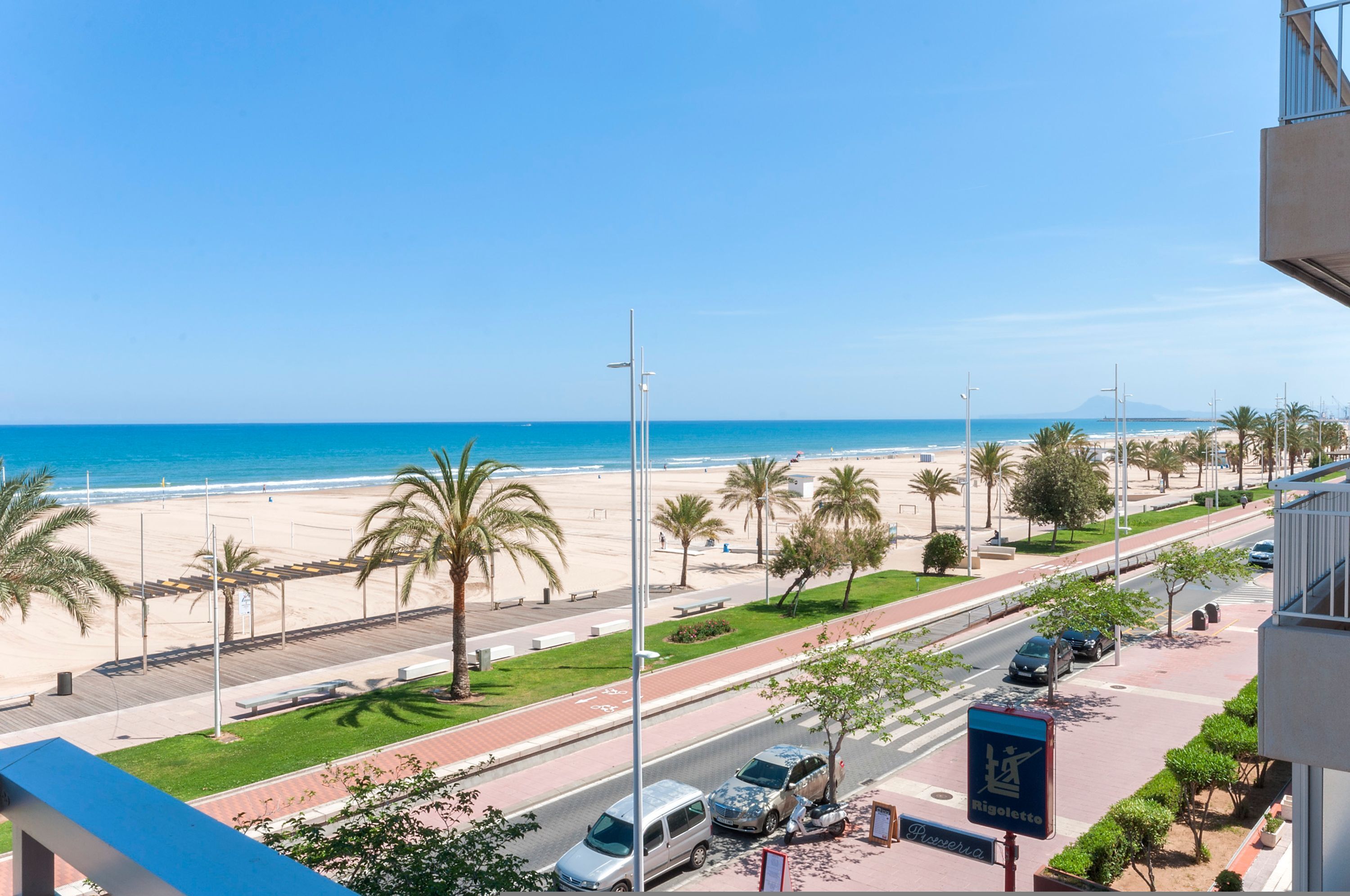 A coastal road with a beach view, palm trees, and a clear sky.