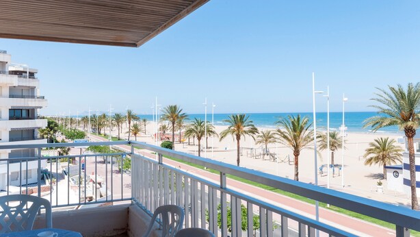 Een balkon met uitzicht op een strand, palmbomen en een heldere lucht.