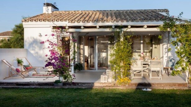 A house with a tiled roof, a covered patio with outdoor furniture, and a garden with flowering plants. - Casa Tecolote in Chiclana de la Frontera (Chiclana de la Frontera)