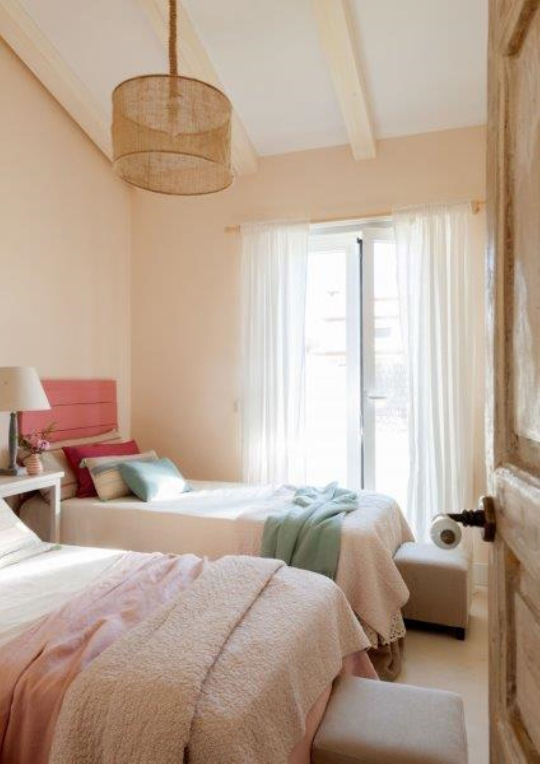 A cozy bedroom with two beds, a bedside table, a hanging light fixture, and a window with curtains.