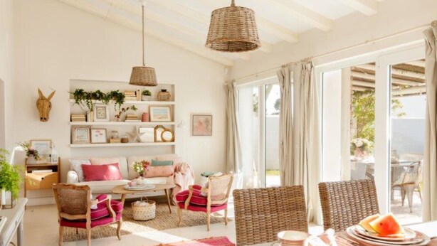A bright, airy living room with a large window, wicker furniture, and a wall adorned with framed pictures and plants. - Casa Tecolote in Chiclana de la Frontera (Chiclana de la Frontera)