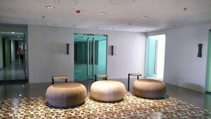 Een moderne lobby met een vloer met geometrisch patroon, drie ronde zithoeken en glazen deuren die leiden naar andere ruimtes.