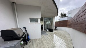 Un patio con una parrilla, una mesita y un espacio cubierto con ventana y puerta.
