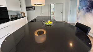 Una cocina moderna con encimera negra, una isla central y una lámpara colgante.