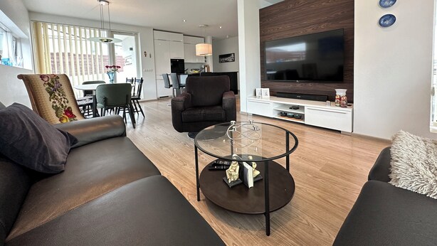 Una sala de estar moderna con un sofá, una mesa de centro de vidrio y un televisor montado en la pared.