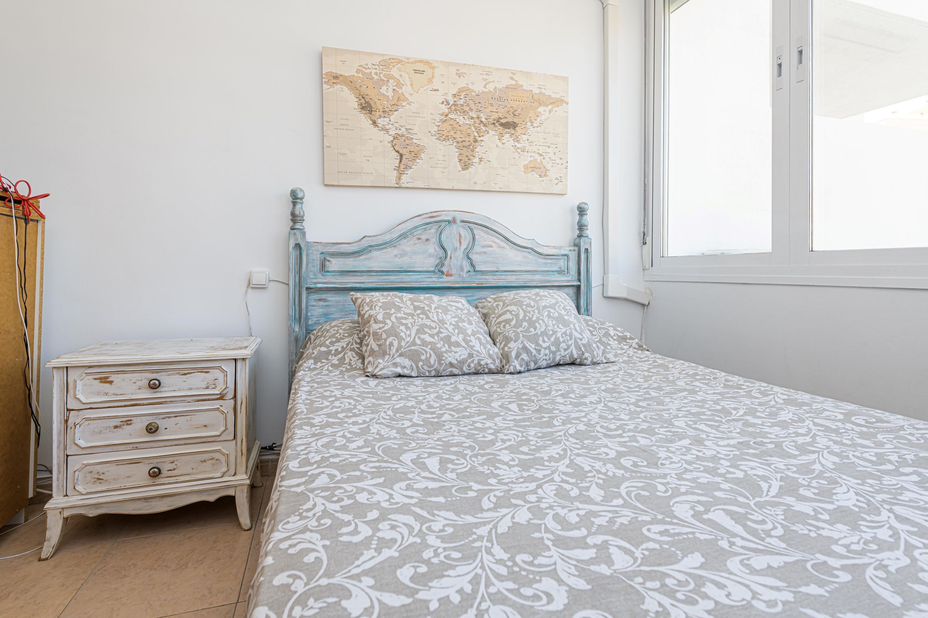 A bedroom with a bed, a dresser, a world map on the wall, and a window.